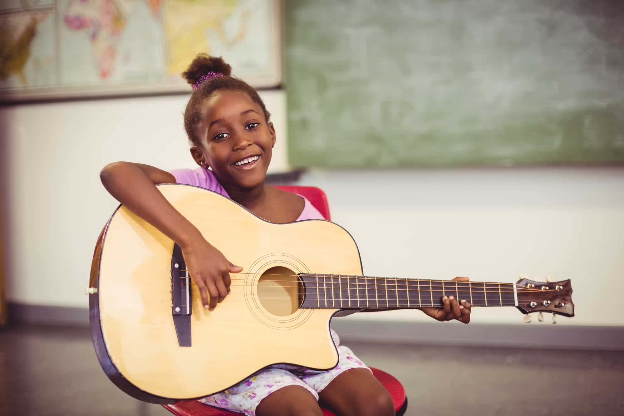 Portrait of smiling schoolgirl playing guitar in classroom Portrait of smiling schoolgirl playing guitar in classroom at school