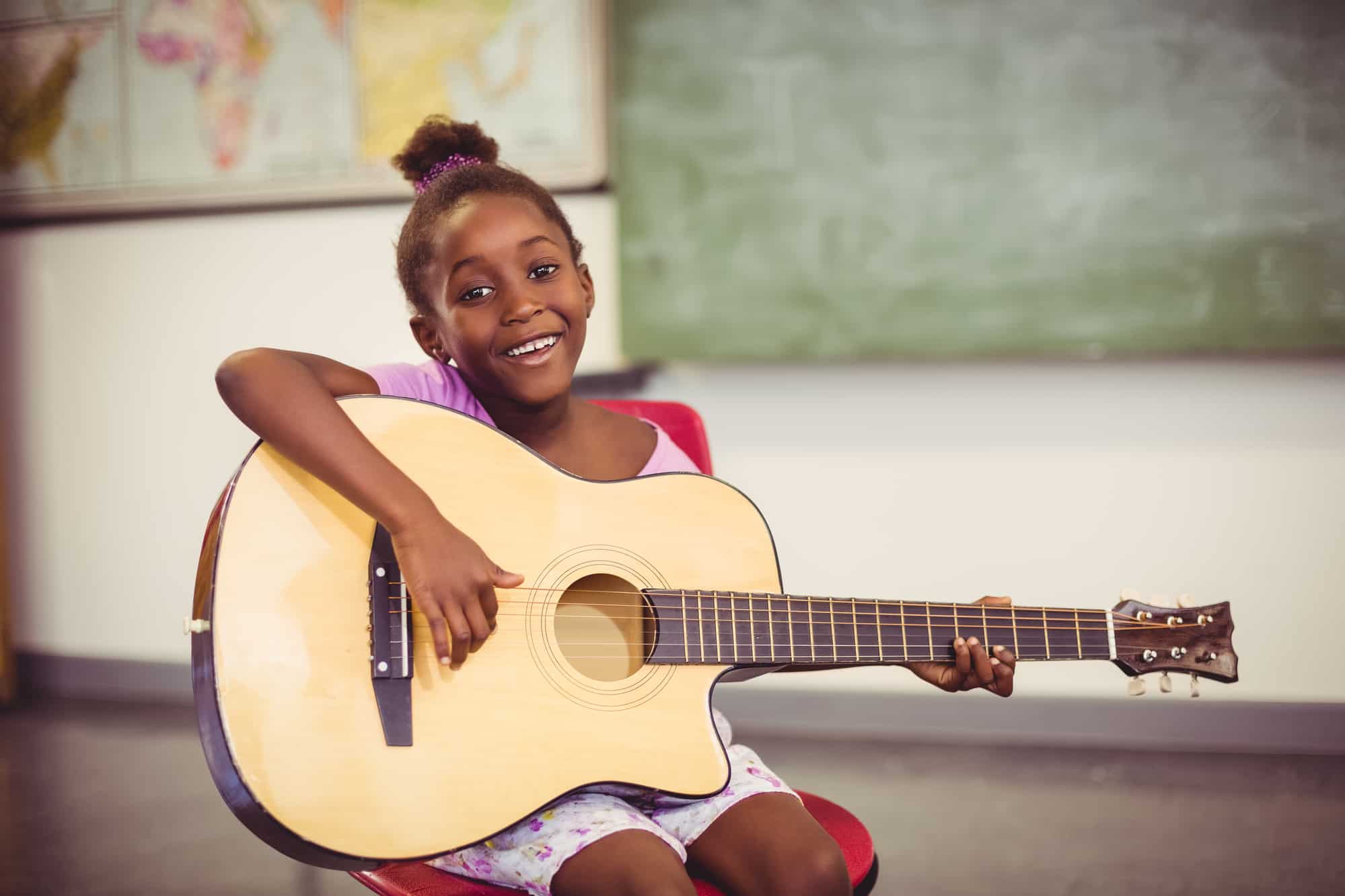 Portrait of smiling schoolgirl playing guitar in classroom at school